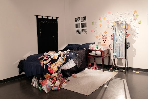 Keira Chu, Viviana Giesbrecht Ferreira,
The Masks We Wear,
2025,
Cot, pillows, blankets, mirror, nightstand, masks, garbage, curtains, rug, dishes, marker, notepad, photographs and posters,
5.8’ x 8’ x 7.5’